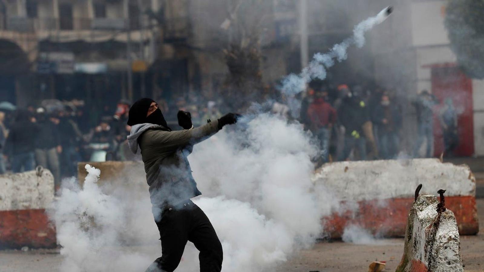 A protester throws back a tear gas canister towards riot policemen during a protest deteriorating living conditions and strict coronavirus lockdown measures, in Tripoli, Al-Arabiya News, January 28, 2021.